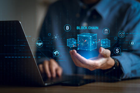 Person in blue shirt uses laptop with holographic blockchain interface.