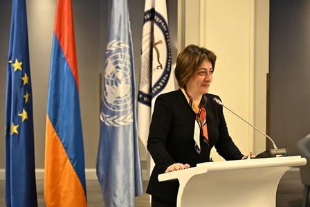 A woman at a podium giving a speech, with EU and UN flags behind her.