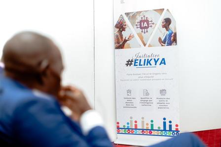 Photograph of a man in a blue shirt seated, studying a poster with graphs on a white wall.