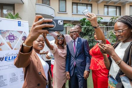 Group of professionally dressed people posing for a selfie outdoors, banner and building in background.