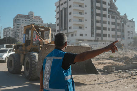 Photo: Construction worker in blue vest points toward a bulldozer on a dusty demolition site.