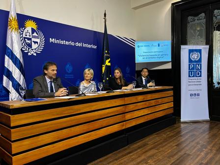 Panel of officials at a press conference with UNDP banner and flags behind.