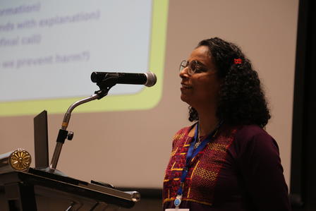Speaker at podium with microphone, presenting in a conference room.