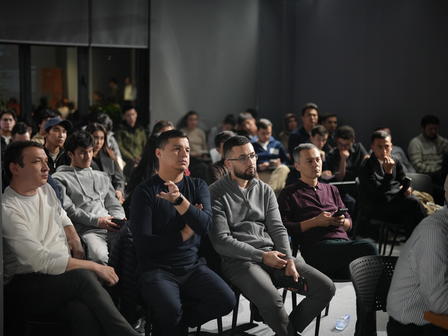 Photograph of a diverse audience seated in a conference room, listening to a speaker.