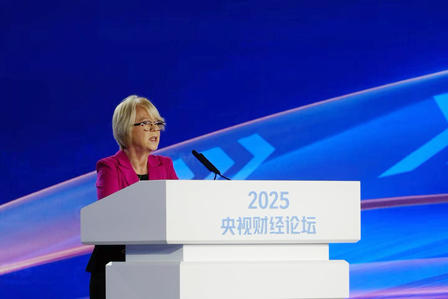 Woman in a pink blazer giving a speech at a white podium on a blue stage.