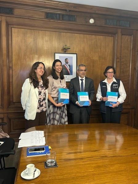 Photograph of five people in a wood-paneled room, holding blue folders.