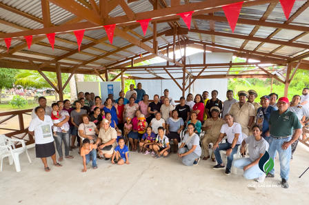 Group photograph under a covered pavilion with red bunting; people pose outdoors by water.