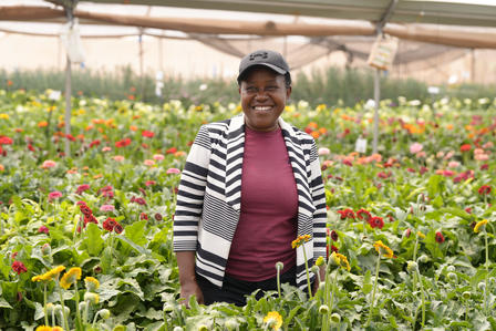 Person standing in a field of colorful flowers, wearing a striped blazer over a maroon top.