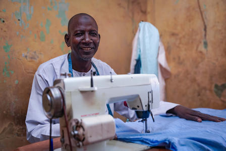 Tailor at a sewing machine stitching blue fabric, orange wall behind