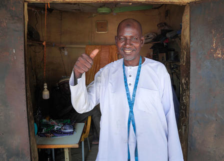 Man in white traditional clothing stands in a weathered doorway with a blue lanyard