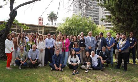Group of people posing on a grassy lawn with trees and tall buildings behind.