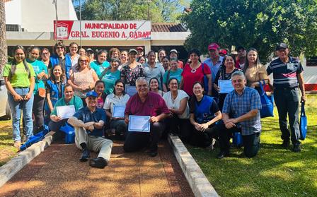 Group photo of people posing outdoors on a sunny lawn in front of a building with a banner.