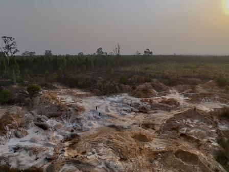 Desolate rocky terrain with white mineral crusts, sparse shrubs, and a setting sun on the horizon.