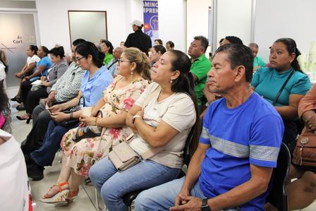 People seated in rows inside a bright room, attending a community meeting.