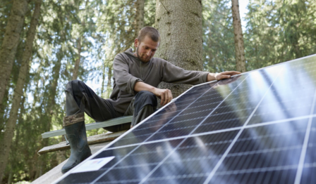 Man crouching on solar panels in a forest, inspecting them.