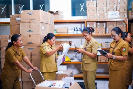 Five workers in tan uniforms sorting supplies in a warehouse with stacked cardboard boxes.