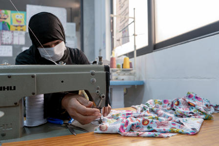 Seamstress wearing a hijab and mask sewing colorful fabric at a Juki sewing machine.