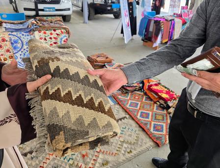 Photograph of two people examining a zigzag patterned rug at an outdoor market.