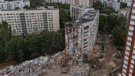 Urban demolition site with partially collapsed high-rise, rubble, and surrounding apartments.