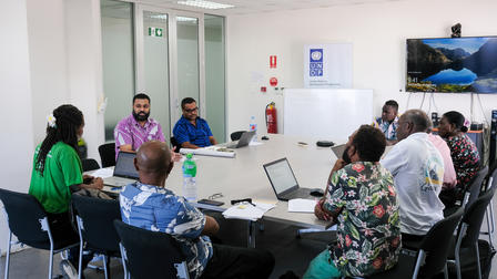 Group of diverse people in a bright office conference room, seated around a table with laptops.
