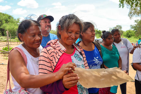 Group of people outdoors under a blue sky, presenting a large beige dried leaf.
