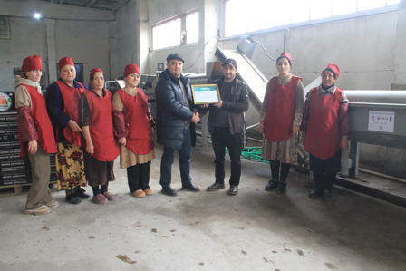 Group of people in red vests in an industrial workshop, one person holding a certificate.