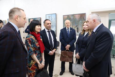 Group of formally dressed people standing in a gallery, with framed photos on walls.