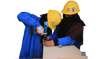 Photograph of two construction workers in yellow helmets working on a wooden board.