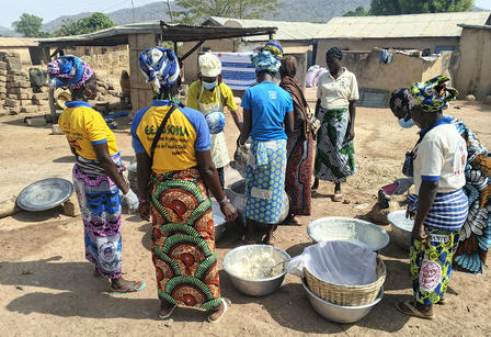 Photo of villagers, mostly women in colorful wraps, gathered around outdoor pots.