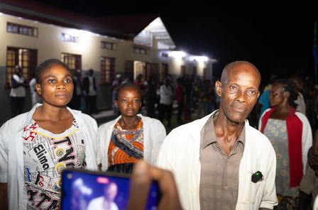 Nighttime photo of people outside a lit venue; foreground man in white shirt.