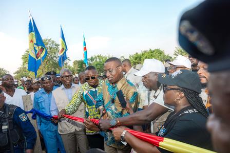 Photograph of a ribbon-cutting ceremony with a diverse crowd, flags, and a red-yellow ribbon.