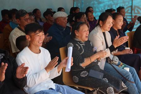 Diverse audience seated indoors, clapping during a presentation.
