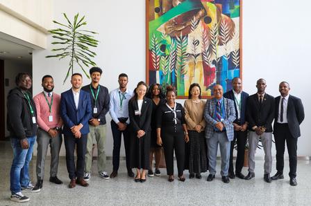 Group of professionals posing for a photo in a modern lobby with a tall plant and a colorful painting.