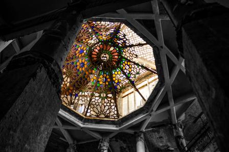 Photograph of a colorful stained-glass dome skylight, framed by dark stone arches.
