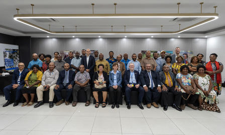 Diverse group posing for a group photo in a conference room, front row seated, back row standing.