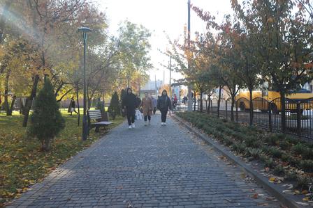 Autumn cobblestone path in a park with people walking away, flanked by trees and lampposts.