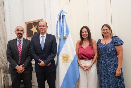 Group photo of two men and two women posing indoors with the Argentine flag between them.