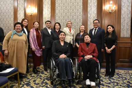 Group photo of people in a wood-paneled conference room; two in wheelchairs.