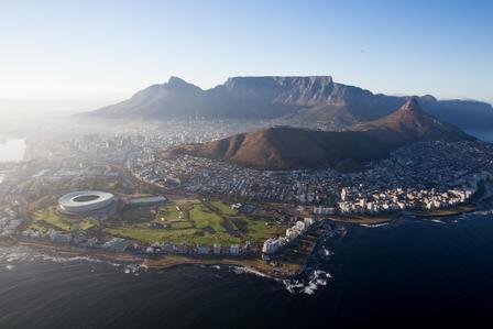 Aerial view of Cape Town: Table Mountain, coastal city, and circular stadium by the shore.