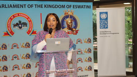 Photograph: woman at podium speaking at Eswatini Parliament event, backdropped by banners.
