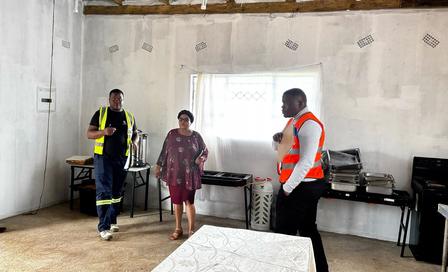Three people in a bare concrete room with stainless grills along the back wall.