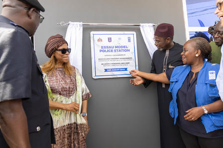 Group of people at an outdoor plaque unveiling, pointing at a framed plaque.