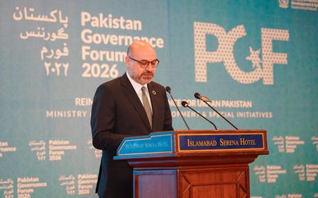 Photograph of a speaker at a podium against a blue backdrop with Pakistan Government Forum banners.