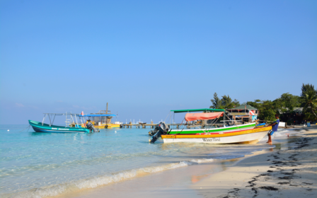 Photo: colorful boats along a sandy tropical beach with turquoise water and blue sky.
