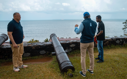Group of people standing by a large black cannon near the sea.