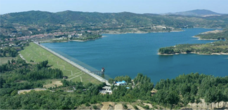 Scenic coastal landscape with a long bridge over blue water, green hills and distant shoreline.