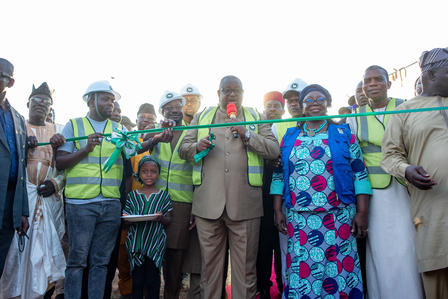 Line of officials and locals holding a green ribbon at a ceremony.
