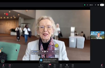 Attendee with a lanyard in a conference lobby; Zoom controls visible.