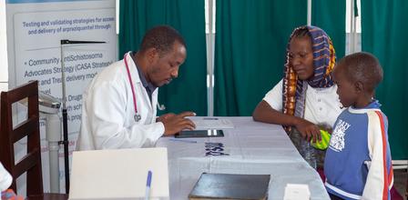 Medical professional in white coat assists a woman and two children at a health fair desk.