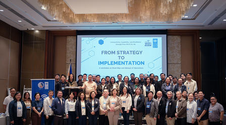 Group of participants on stage at a conference, screen reads From Strategy to Implementation.